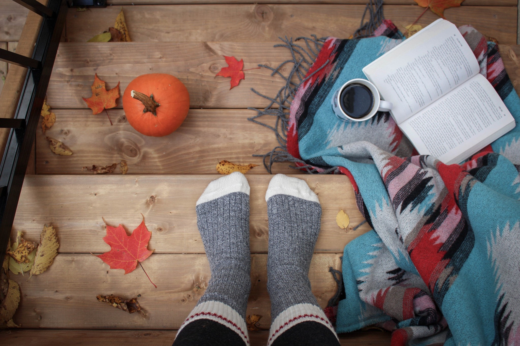 Practicing self-care in the fall with warm socks, a book, coffee, blanket, pumpkins and leaves.